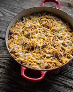 a casserole dish with cheese and other toppings in a red pan on a wooden table