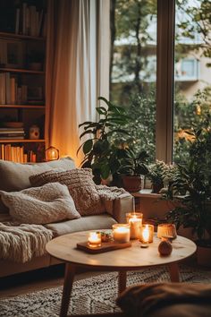 candles are lit on the coffee table in front of an open window with bookshelves and potted plants