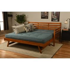 a wooden futon bed with blue mattress and pillows on it in a living room