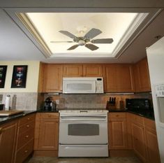 a ceiling fan in a kitchen with wooden cabinets and white stove top oven, microwave and dishwasher