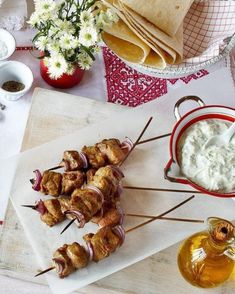 skewers of meat and vegetables are served on skewers next to a bowl of dip