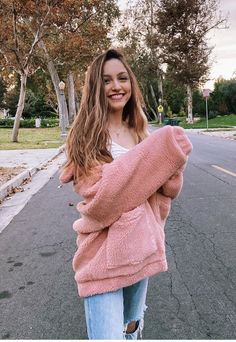 a woman standing in the street wearing a pink fuzzy sweater and ripped jeans with her hands on her hips