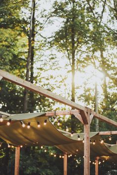 the sun is shining through the trees and lights are hanging from the wooden structure in front of the gazebo