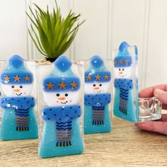 four snowmen in blue hats and scarfs are sitting on a table next to a plant