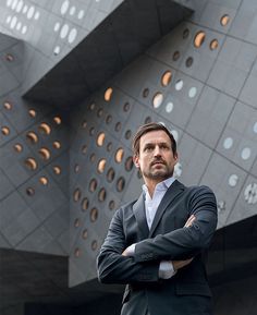 a man standing in front of a building with his arms crossed and looking at the camera