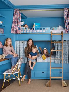 a woman and two children are sitting on a bunk bed in a room with blue walls