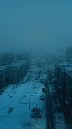 an empty city street covered in snow during the wintertime with cars parked on it