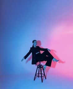 a woman sitting on top of a stool in front of a pink and blue background