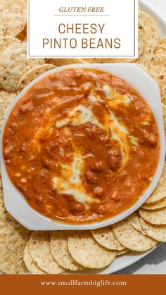 a white plate filled with cheesey pinto beans and tortilla chips on the side