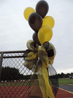 a bunch of balloons tied to a fence with a yellow bow on the top and bottom