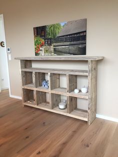 a wooden shelf sitting on top of a hard wood floor next to a painting and vases