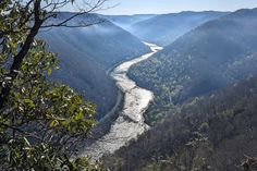 a river flowing through a valley surrounded by mountains in the middle of the day with trees on both sides