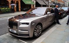 two men standing next to a silver rolls royce parked on the side of a street