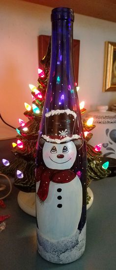 a glass bottle with a snowman on it sitting next to a christmas tree in the background