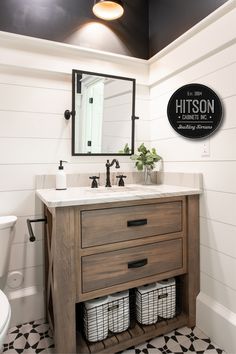 a bathroom with black and white tile flooring and a wooden vanity topped with two baskets under a mirror