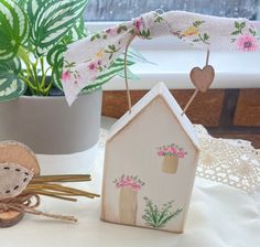 a doll house next to a potted plant and some scissors on a table with lace