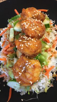 a black plate topped with shrimp and veggies covered in sesame seed sprinkles