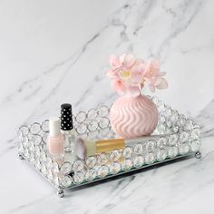 a pink vase sitting on top of a glass tray filled with nail polish and cosmetics