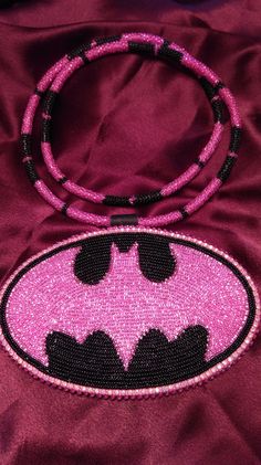 a pink and black beaded batgirl purse on a purple satin background with the word batman written across it