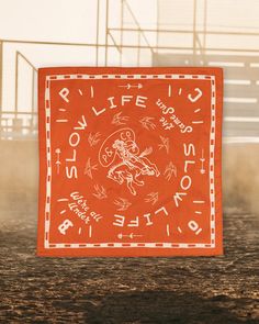 an orange bandana with white writing on it in front of a dirt ground area