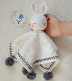 a crocheted bunny doll is held by someone's hand on a white blanket