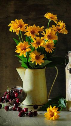 yellow daisies and cherries are in a vase next to an old milk can