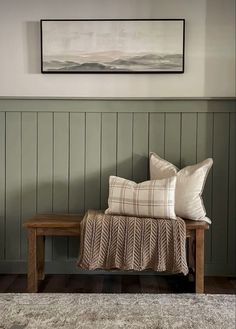 a wooden bench with two pillows on it in front of a green paneled wall