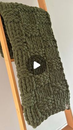 a green blanket on top of a wooden ladder next to a white wall with a black hole in the middle