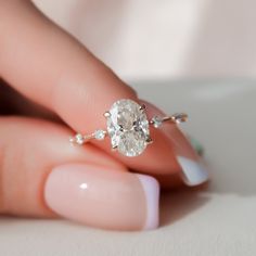 a woman's hand holding an oval diamond ring