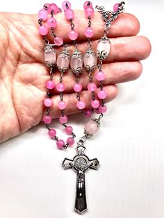 There are 59 total beads in this five decade rosary. The rosary has a 2 Inch Silver Plated St. Benedict Crucifix that is beautifully detailed on both sides. The center is an antiqued silver plated fancy scrolled 3-way. This rosary is wired wrapped with very nice 6 mm faceted pink jade in unbreakable fashion. There are 24 silver plated bead caps that protect the beautiful Rose Quarts Oval Beads that represent the Pater (Our Father) Beads. ROSE QUARTZ: The fair and lovely Rose Quartz, with its gen Spiritual Rosary With Spacer Beads, Handmade Pink Rosary For Healing, Pink Beaded Spiritual Rosary, Pink Rosary With 8mm Round Beads, Pink Spiritual Rosary Bracelet With 8mm Beads, Pink Beaded Rosary With Round Beads, Pink Healing Rosary With 8mm Beads, Pink 8mm Bead Spiritual Rosary Bracelet, Pink 8mm Beads Rosary Bracelet