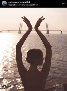 a woman standing in front of the water with her hands up and arms raised above her head