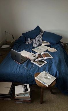 an unmade bed with many books on it and a laptop sitting on the end table