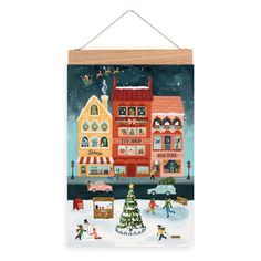 a christmas card hanging on a wall next to a tree and snow covered street with buildings