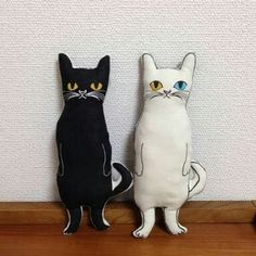 two black and white cats sitting next to each other on a wooden shelf in front of a wall