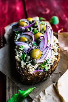 an open face sandwich with onions and olives on it sitting on wax paper next to some green peppers