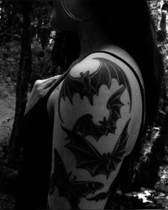 a woman with a bat tattoo on her arm and shoulder is looking at the woods