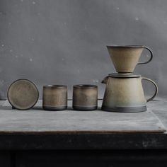 three coffee pots and two cups sitting on top of a table