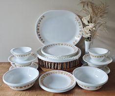 a table topped with plates and bowls on top of a wooden table next to a vase filled with flowers