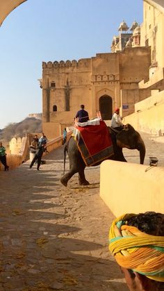 people riding on the backs of elephants in front of an old city wall and gate