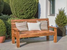 a wooden bench sitting in front of some bushes and potted plants on the ground