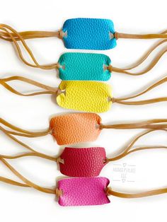 four different colors of leather hair clips hanging on a wooden stick in front of a white background