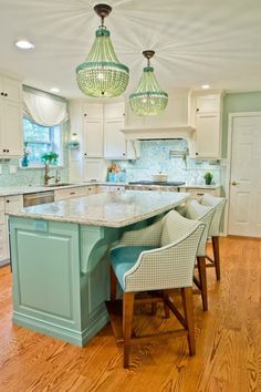 a large kitchen with an island in the center and two hanging lights above it, along with wooden flooring