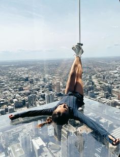 a man hanging upside down on a glass floor in front of a cityscape