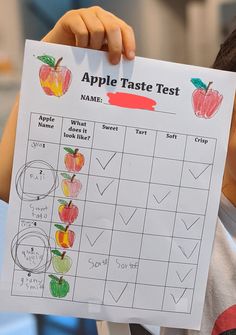 a young boy holding up a paper with an apple taste test written in front of him