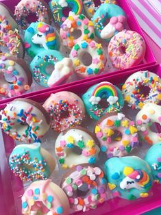 two pink boxes filled with donuts covered in sprinkles and rainbow colored frosting