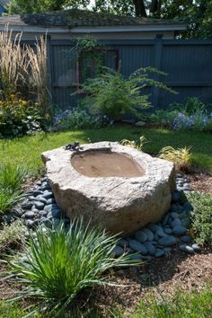 an outdoor fire pit in the middle of a yard with rocks and plants around it