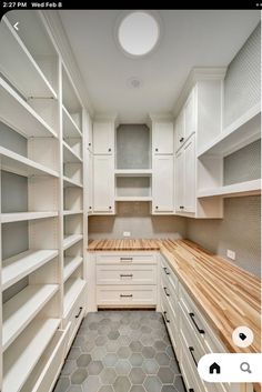 a large walk in closet with white cabinets and wood counter tops, along with hexagonal tile flooring