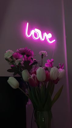 a vase filled with pink and white flowers next to a neon sign that says love