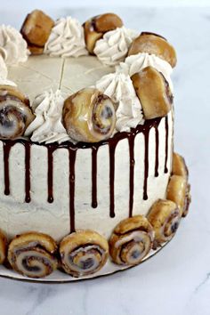 a white cake with chocolate icing and cinnamon rolls around it on a marble surface