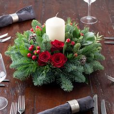 a christmas centerpiece with red roses, greenery and candles on a wooden table